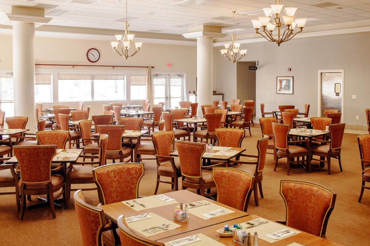 An elegant dining room with neatly arranged tables and chairs, illuminated by chandeliers.