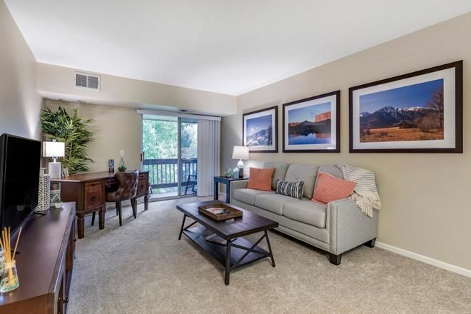 A cozy living room with a sofa, coffee table, and wall art, leading to a dining area and balcony.