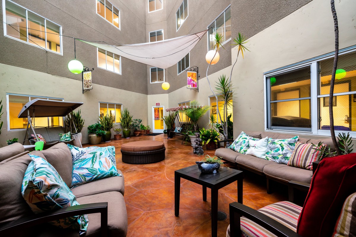 A cozy indoor patio featuring seating areas with cushions, surrounded by plants and modern decor.