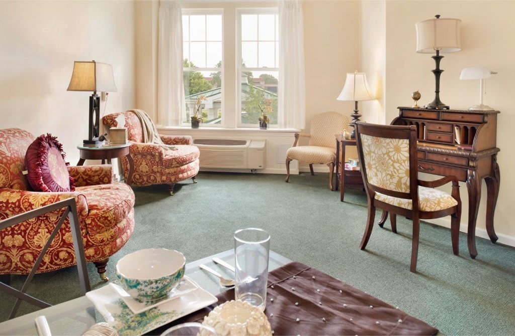 A cozy living room with plush armchairs, elegant lamps, and a large window allowing natural light.