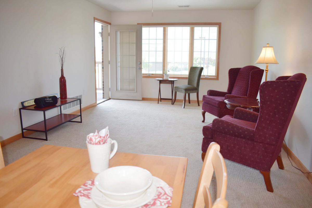 A cozy living room featuring armchairs, a small table by the window, and a dining area with a neatly set table.