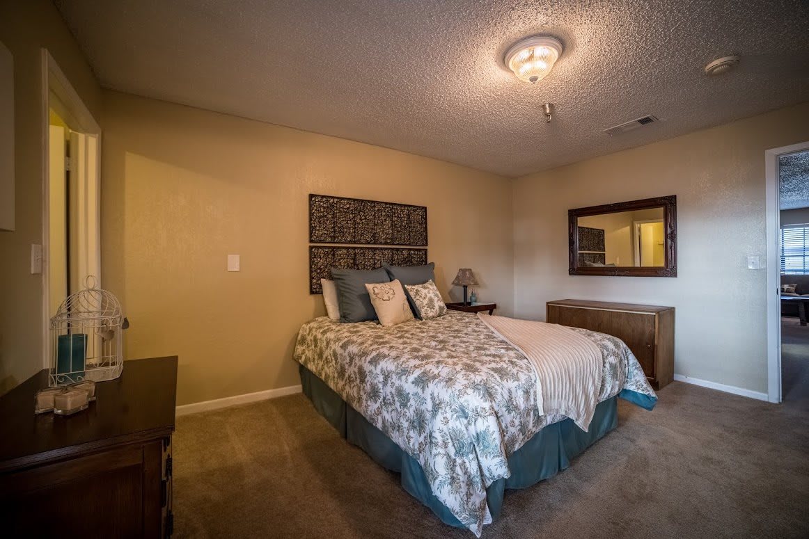 A cozy bedroom with a decorated bed, a mirror, and warm lighting.