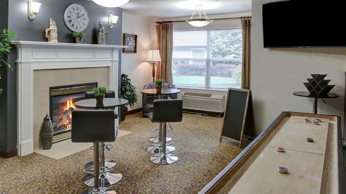 A cozy and modern seating area with tables, chairs, a fireplace, and natural light coming through a large window.