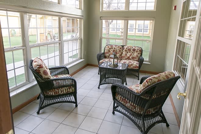 A cozy sunroom featuring wicker armchairs and a coffee table with floral cushions.