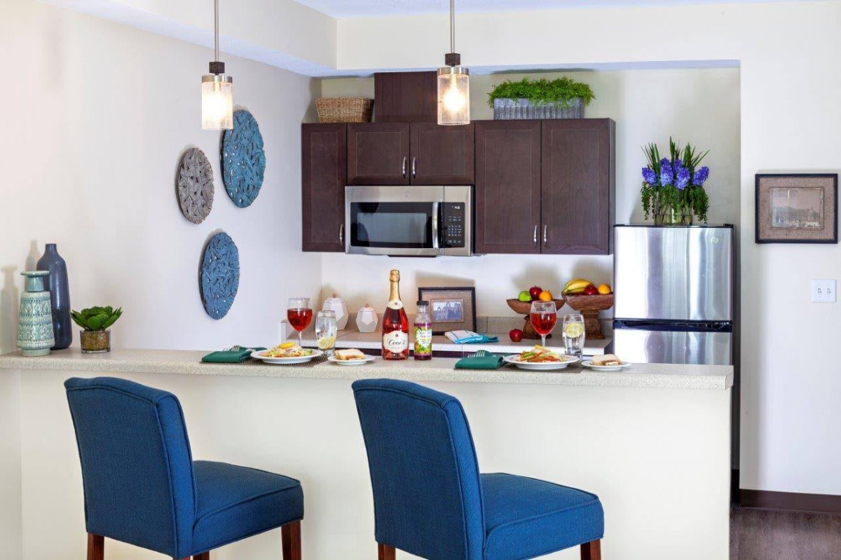A modern kitchen interior featuring a countertop with blue bar stools, pendant lights, and a dining setup.