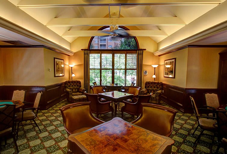 A luxurious lounge area with wooden tables and comfortable armchairs, illuminated by warm lighting.