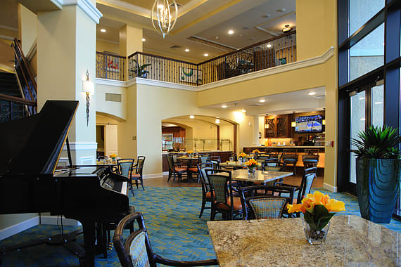 A modern dining area with a grand piano, featuring elegant furniture and bright lighting.