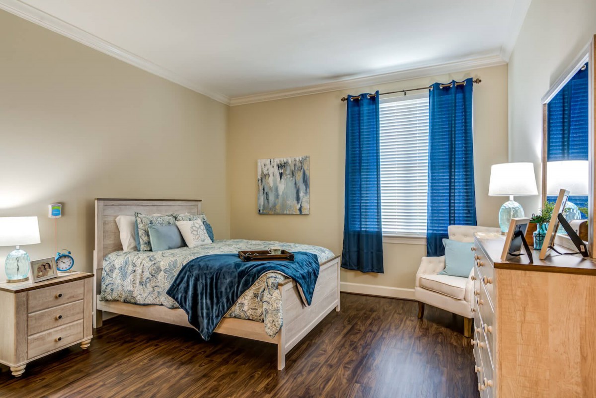 A cozy bedroom featuring a wooden floor, blue curtains, and coordinated bedding.