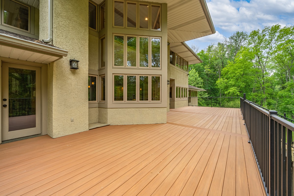 A modern house with an expansive wooden deck overlooking a lush, green landscape.