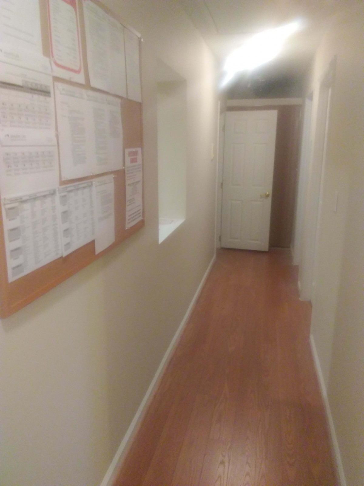 A narrow hallway with a notice board on the wall and a door at the end.