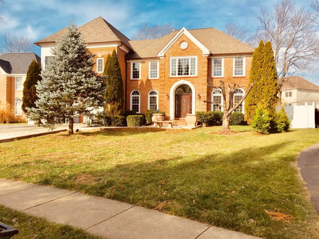A large suburban brick house with a well-maintained lawn and surrounding trees.