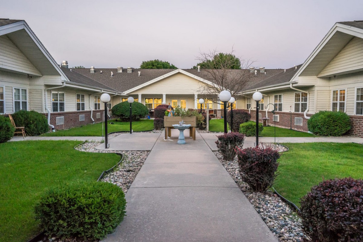 A well-maintained building exterior with a paved pathway, surrounded by lush greenery and outdoor lighting.