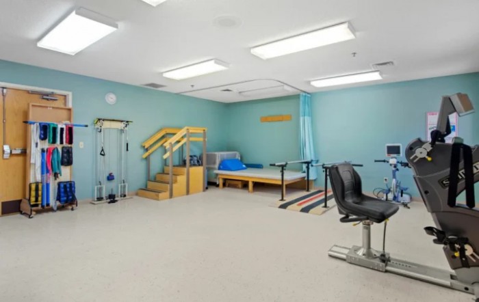 A physical therapy room equipped with exercise machines, parallel bars, and a staircase for rehabilitation exercises.