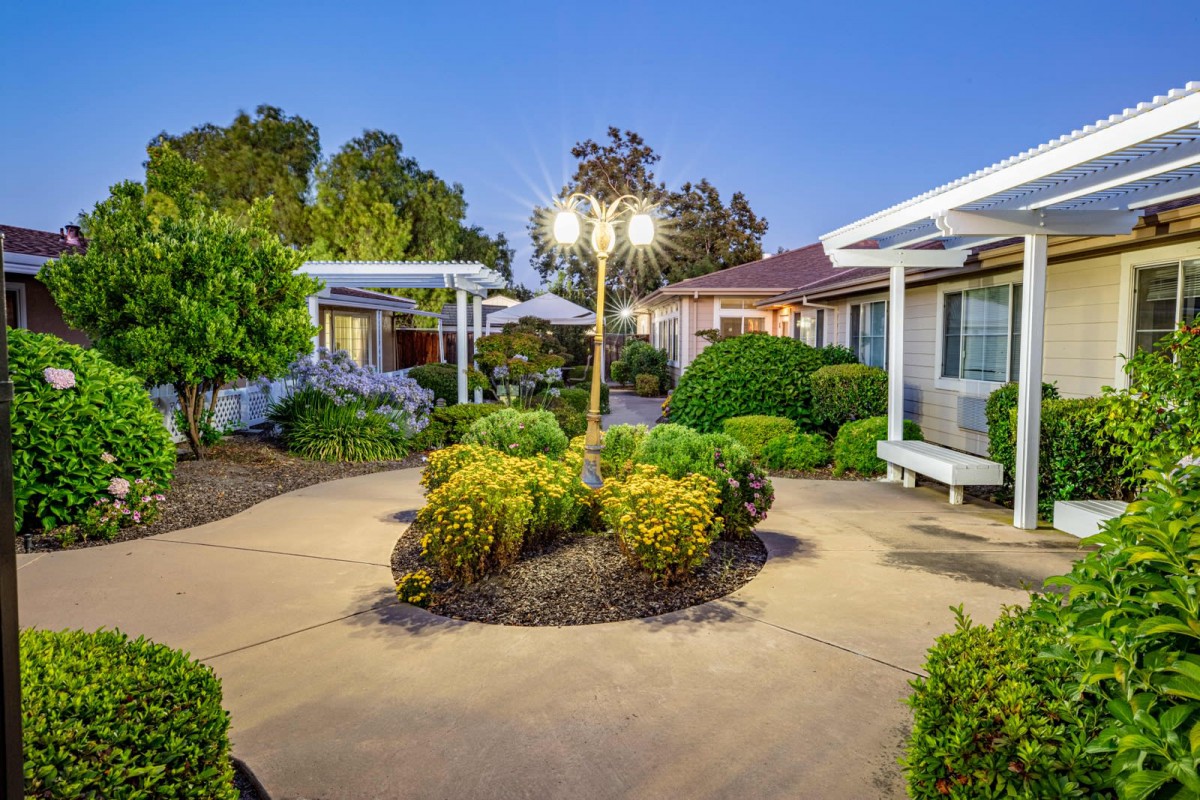 A well-lit courtyard garden with manicured bushes and a central lamp post during the evening.