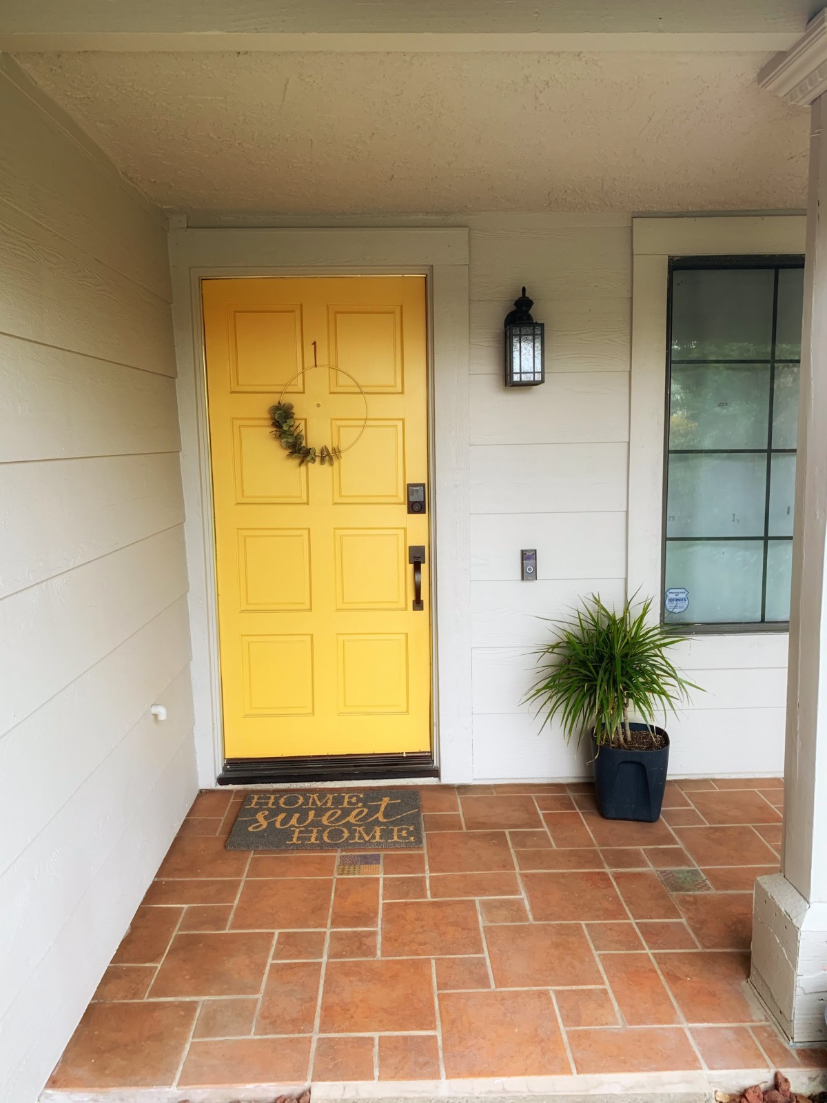 A welcoming front porch with a bright yellow door and potted plant.