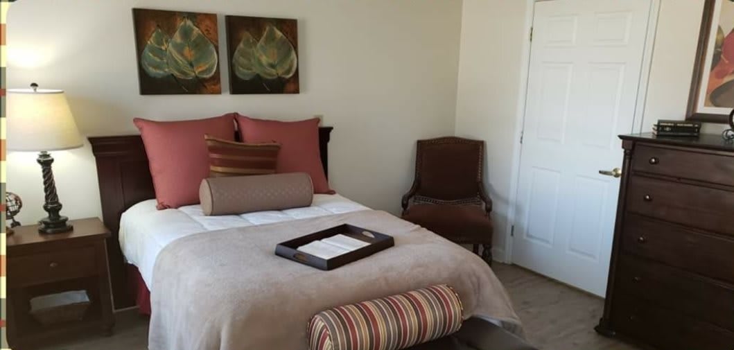 A cozy, well-decorated bedroom with artwork above the bed and a cushioned chair in the corner.