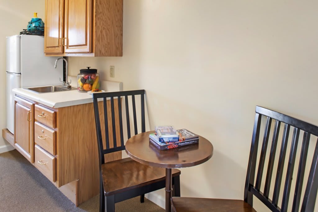 A small kitchen area with a round table, two chairs, and wooden cabinets.