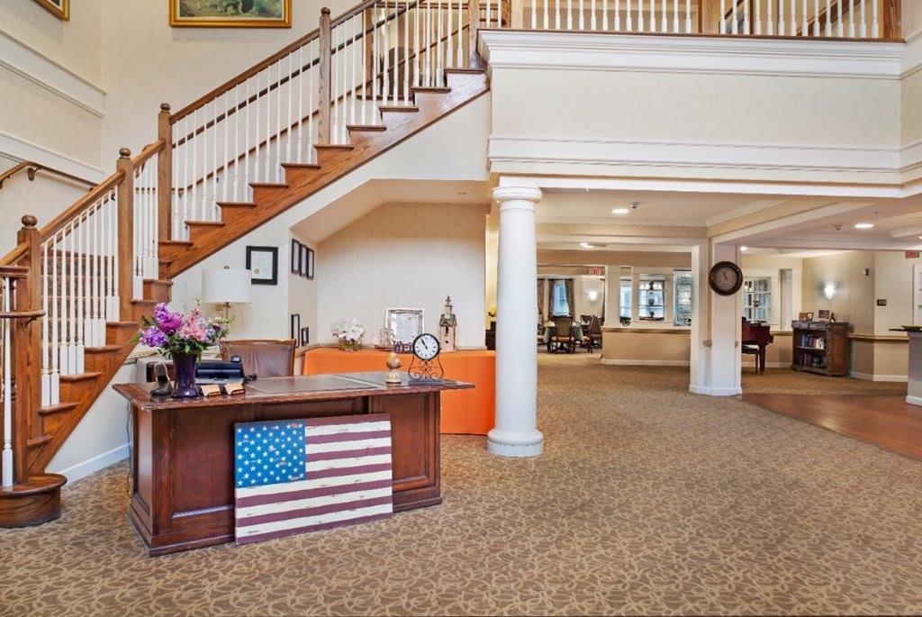 A welcoming lobby features a reception desk adorned with an American flag, leading to a staircase and open common area.