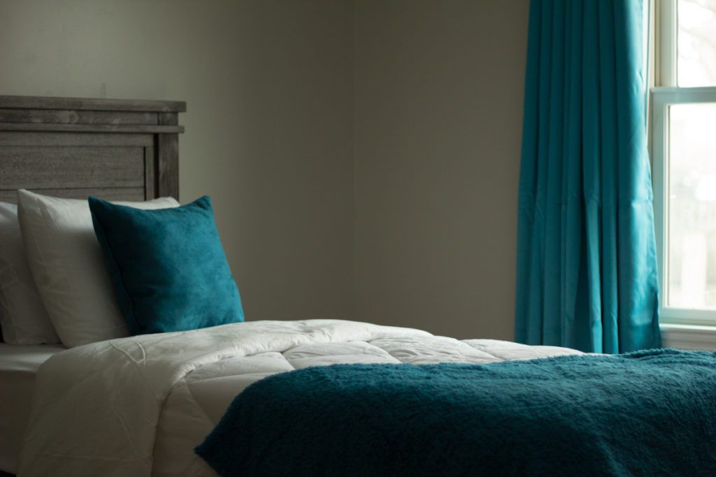 A cozy bedroom with a teal color scheme featuring a neatly made bed and matching curtains.