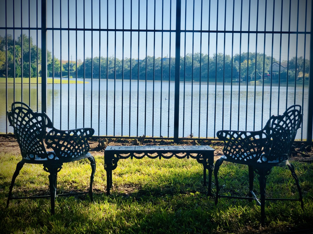 Two ornate benches facing a tranquil lake behind a fence.