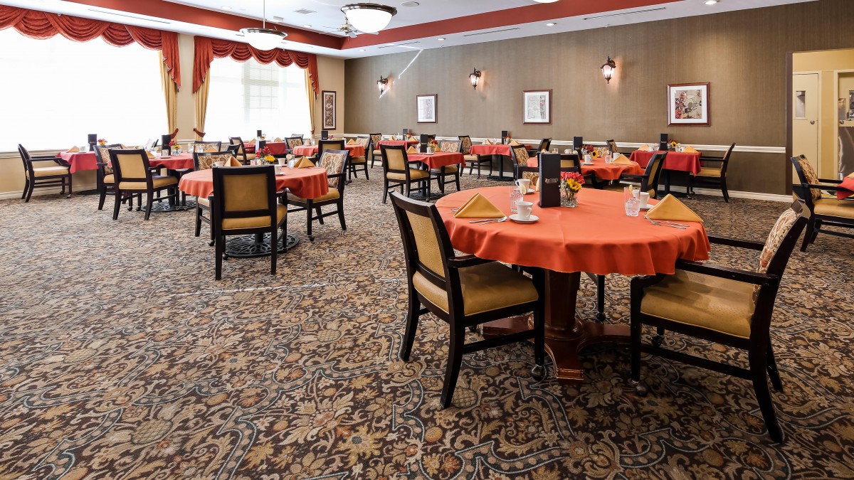 A well-decorated dining room with multiple tables and chairs, featuring warm colors and elegant lighting.