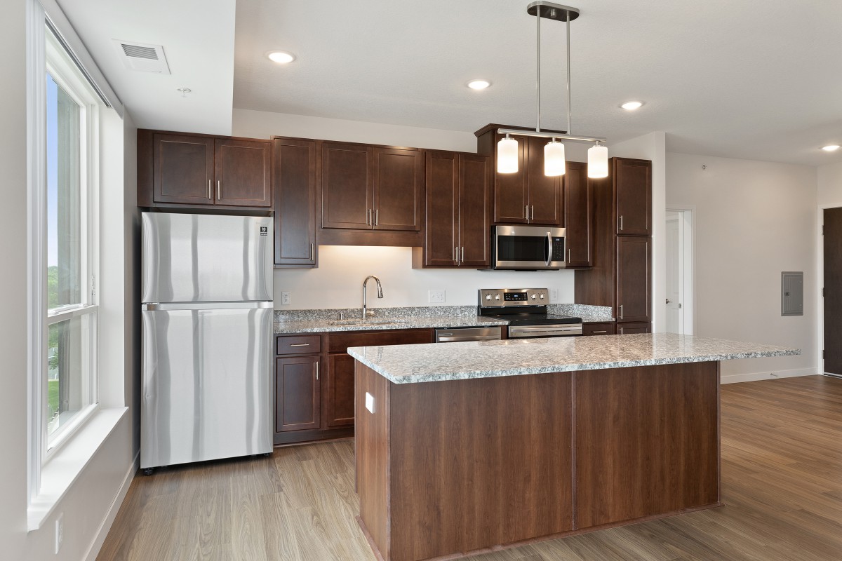 A modern kitchen with wood cabinets, stainless steel appliances, and a central island with pendant lighting.