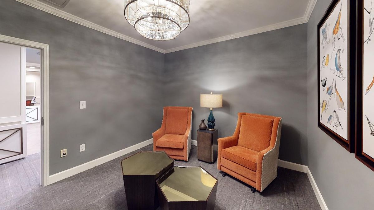 A modern living room with two orange chairs, a lamp, and geometric tables under a chandelier.