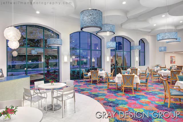 A modern restaurant interior featuring colorful flooring and large arched windows.