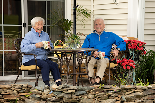 An elderly couple enjoys their time together in a serene outdoor setting, sipping tea by the garden.