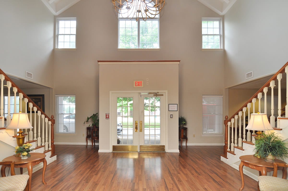 A spacious lobby with a chandelier, featuring wood flooring and large windows.