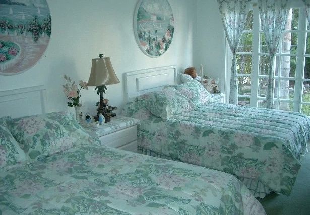 A serene bedroom featuring two twin beds with floral bedding, a bedside table with a lamp, and a window adorned with curtains.