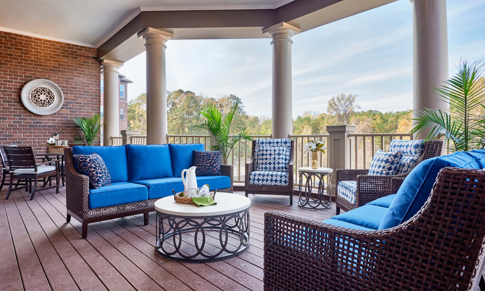 A stylish outdoor patio with blue cushioned furniture and a round table, set against a backdrop of lush greenery.