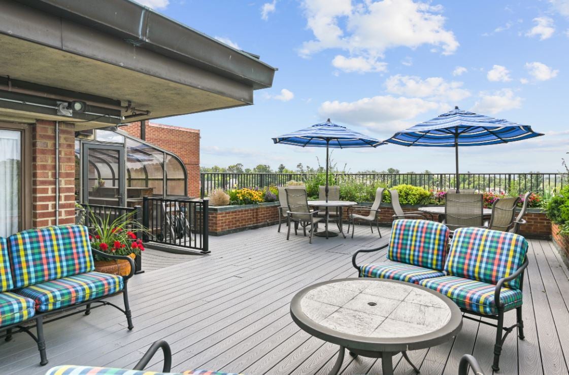 A rooftop patio with outdoor seating, umbrellas, and a view of the cityscape under a clear sky.