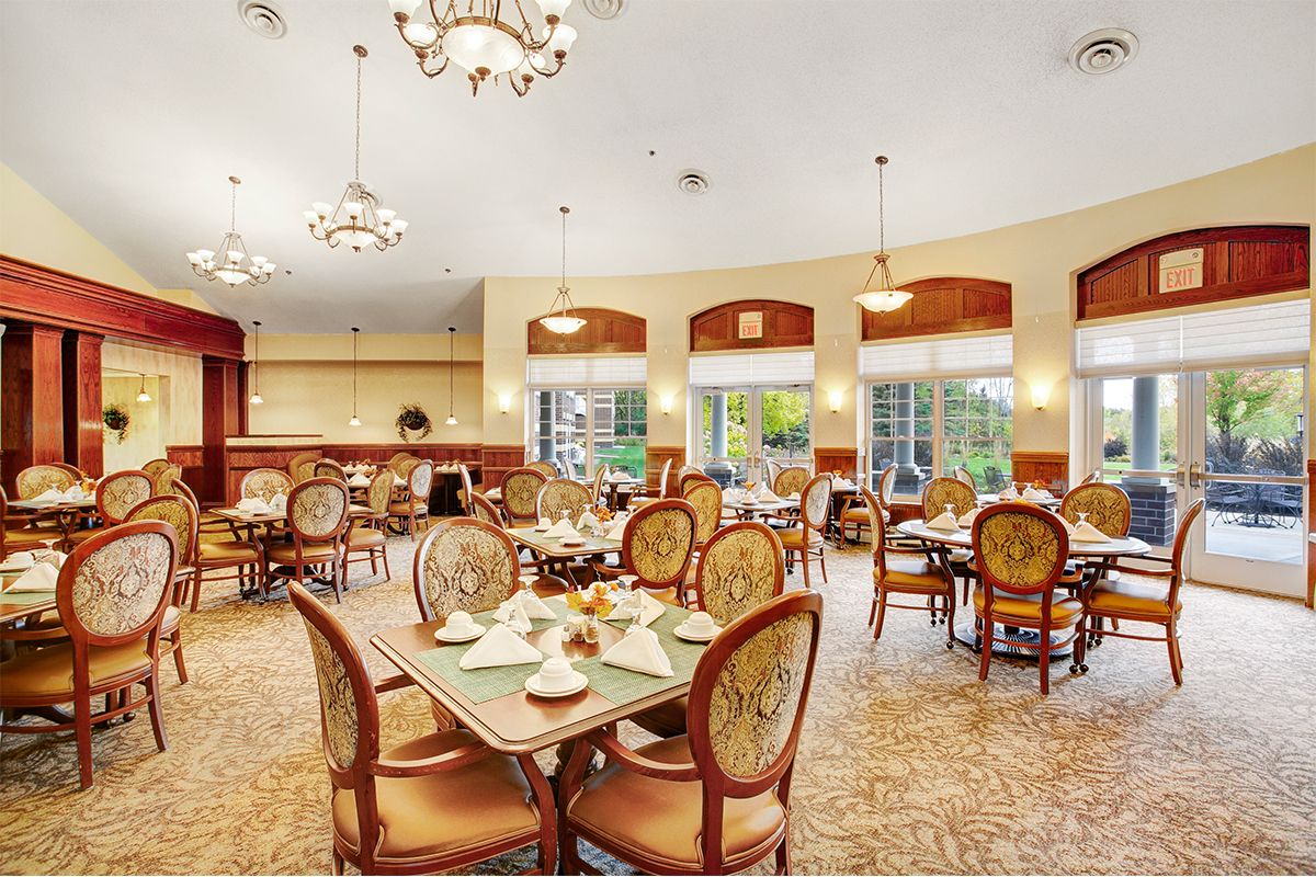 An elegant dining room with ornate chandeliers, set for guests, featuring natural lighting and cozy decor.