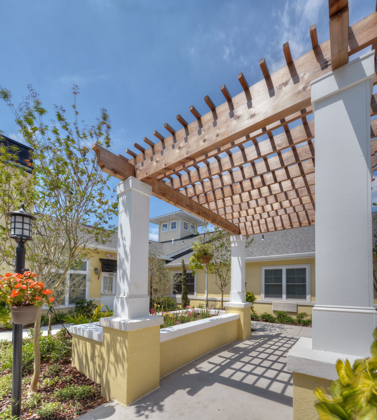 A sunny outdoor space featuring a wooden pergola and lush garden surroundings.