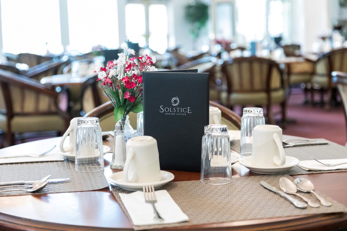 A neatly set dining table with a menu, glasses, cups, and fresh flowers.