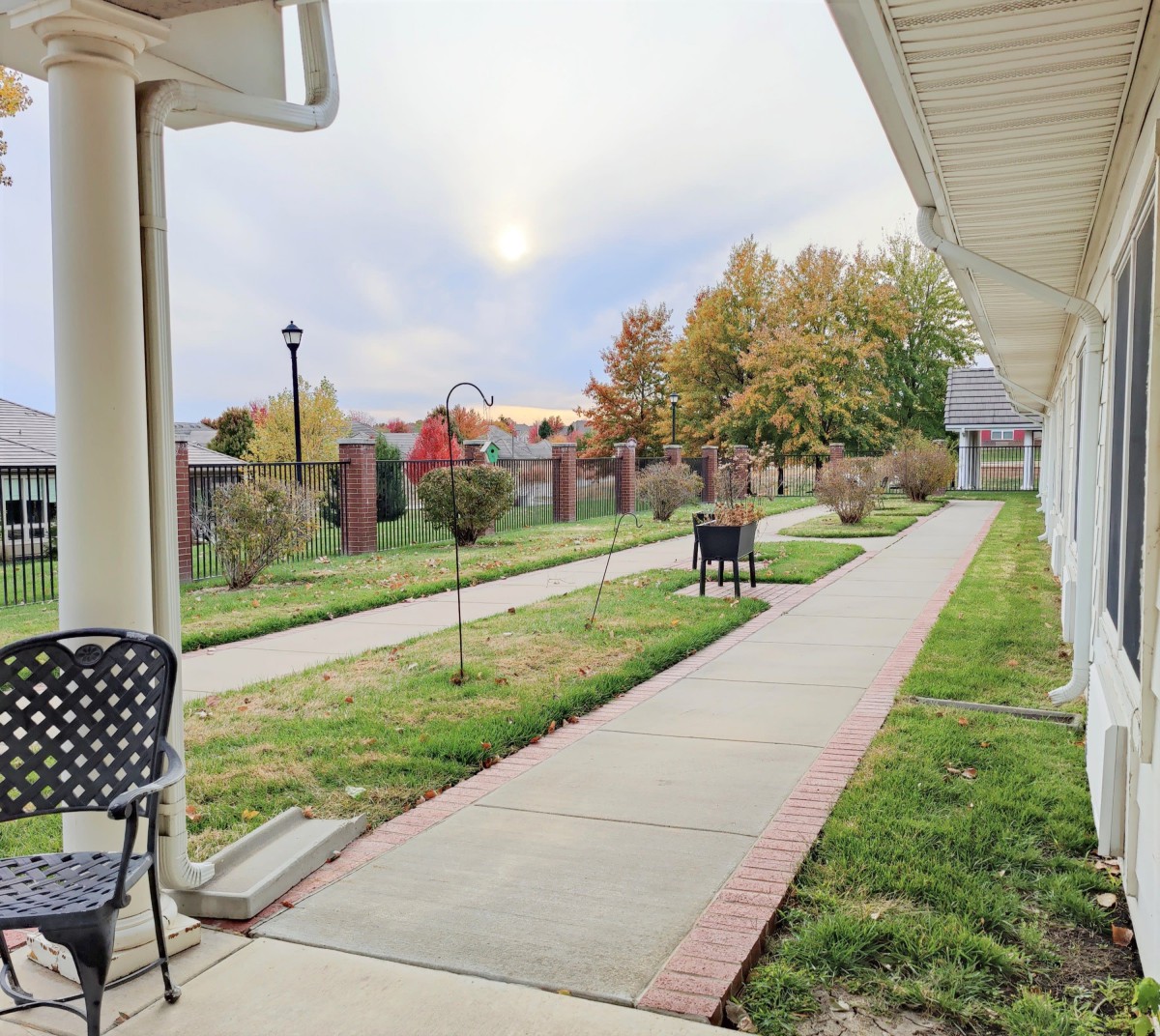 A peaceful garden walkway lined with trees and chairs under an early evening sky.