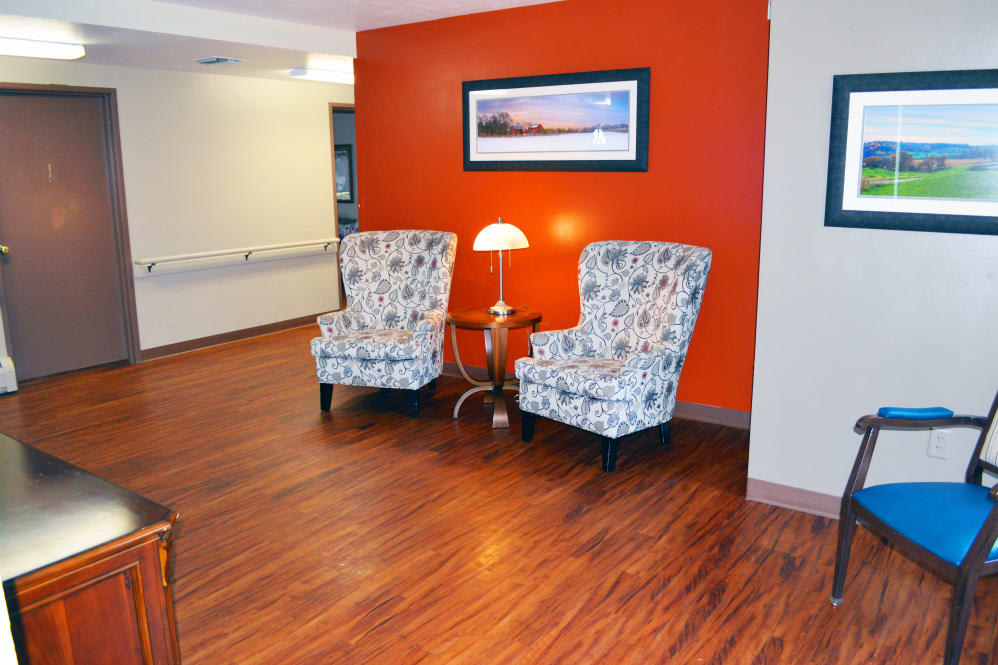A cozy seating area with two patterned chairs, a lamp, and artwork on an orange wall.