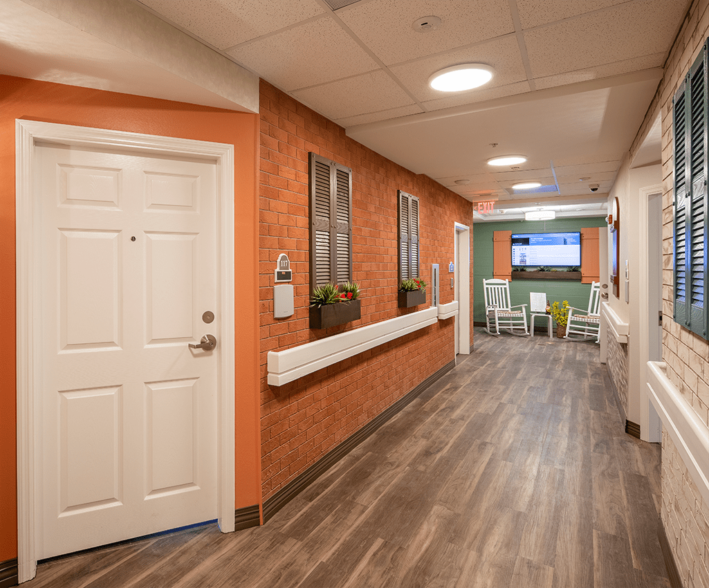 A warmly decorated hallway in a nursing home with orange walls and wood flooring.