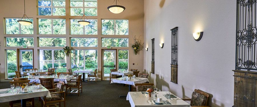 A cozy restaurant interior with several dining tables and large windows providing a view of greenery outside.