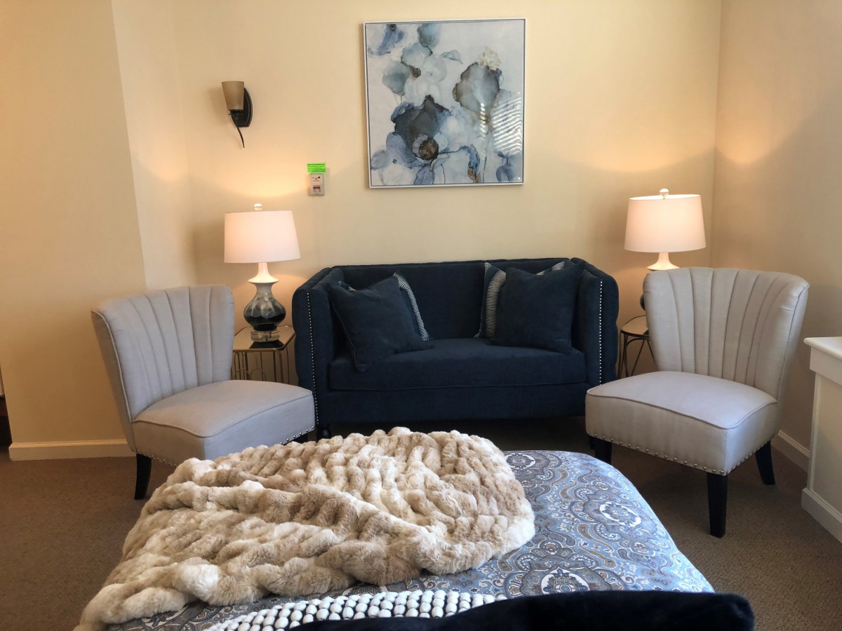 A cozy living room with a dark blue sofa, two armchairs, lamps, and abstract wall art.