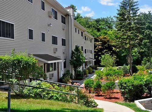A well-maintained apartment building surrounded by lush greenery and landscaped gardens on a sunny day.