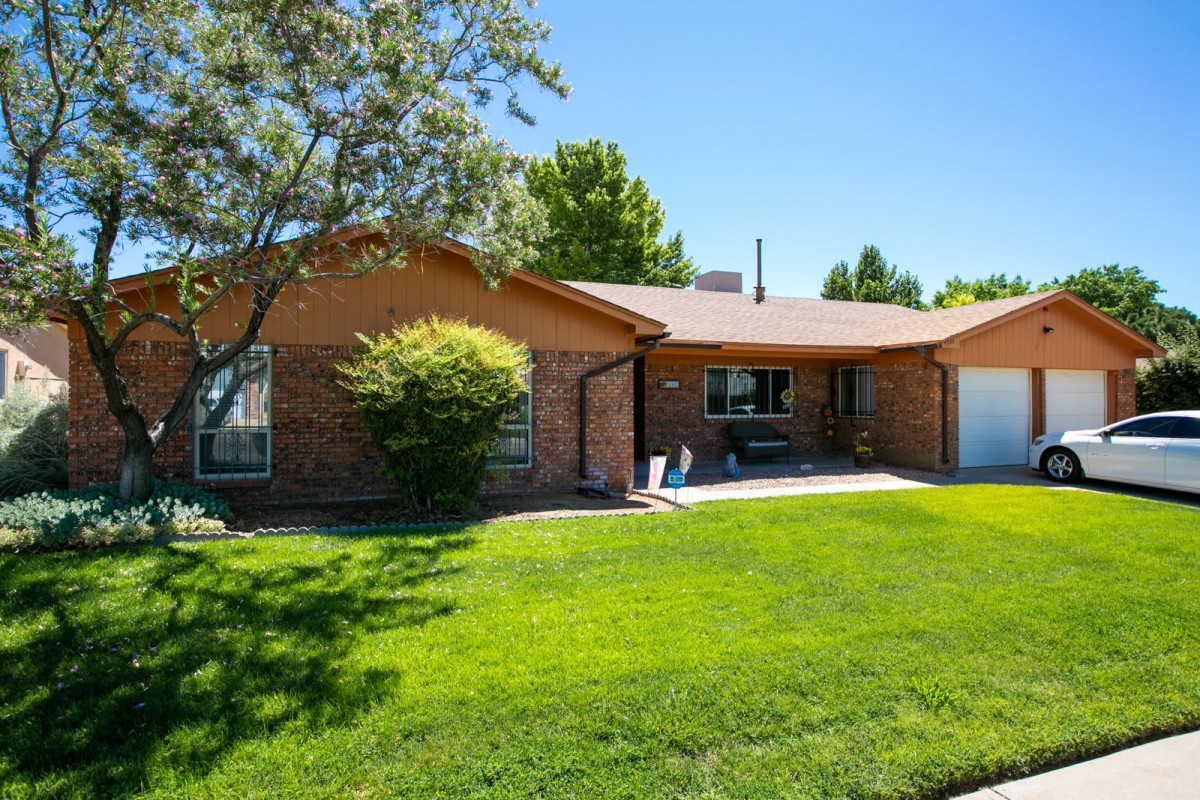 A suburban brick house with a well-maintained lawn and trees on a sunny day.