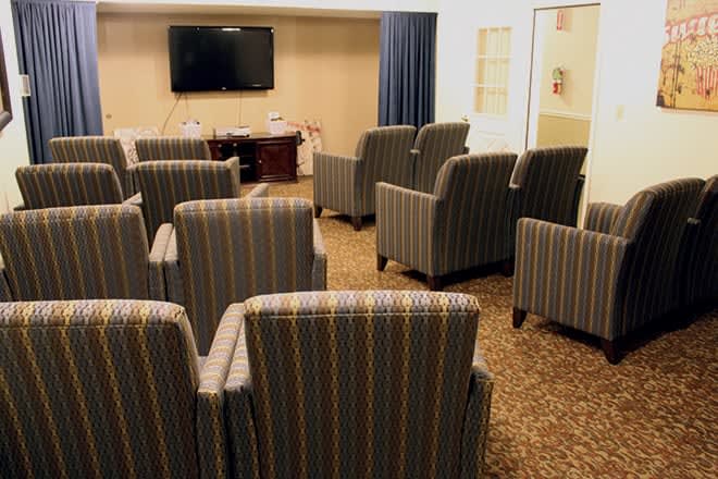 A conference room with multiple upholstered chairs facing a television on the wall.