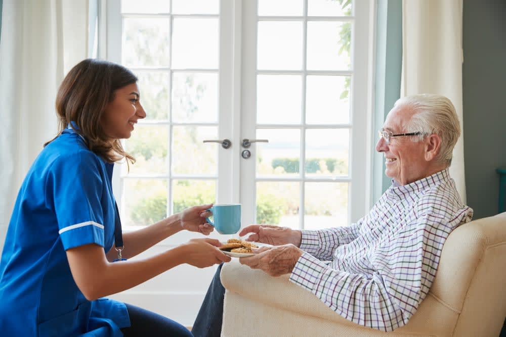 Caregiver offering a drink to an elderly man in a comfortable home setting.