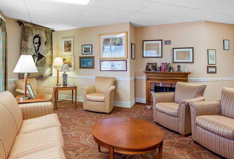 A cozy living room with armchairs and a coffee table, decorated with artwork and a fireplace.