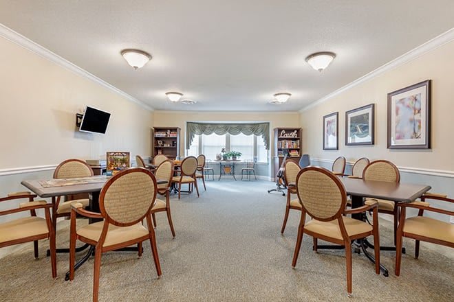 A spacious meeting room with tables, chairs, and bookshelves under soft lighting.