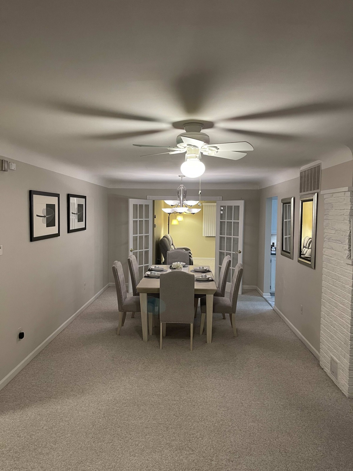 A modern dining room with a table set for six, featuring a ceiling fan and contemporary artwork.