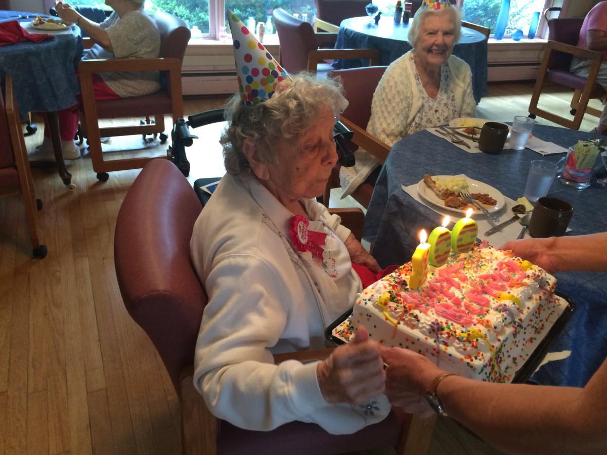 An elderly woman enjoys her birthday celebration with a cake adorned with candles.