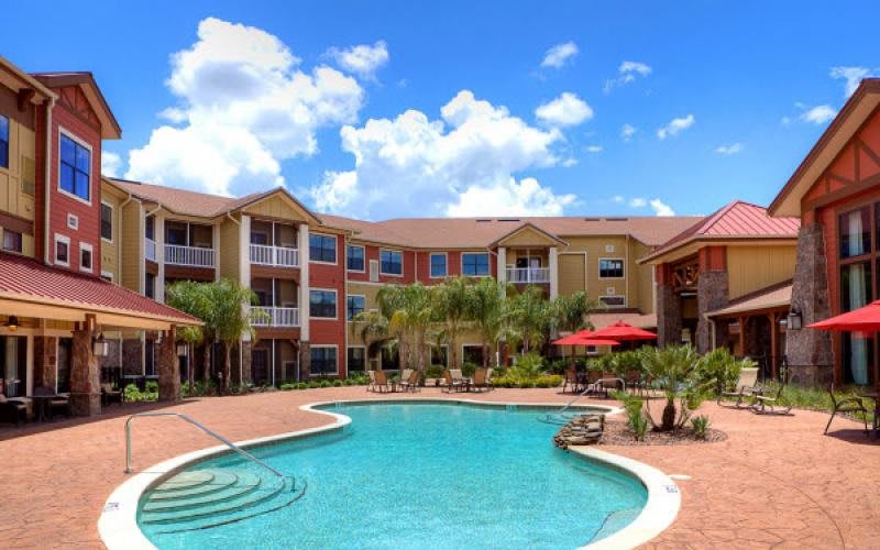 A sunny day at an apartment complex with a spacious pool and surrounding palm trees.